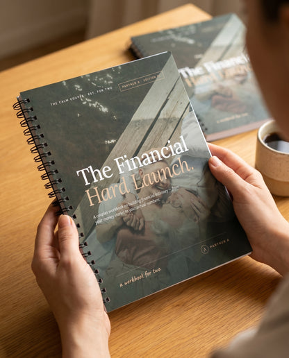 Hands holding the spiral-bound The Financial Hard Launch couples workbook at a cozy desk